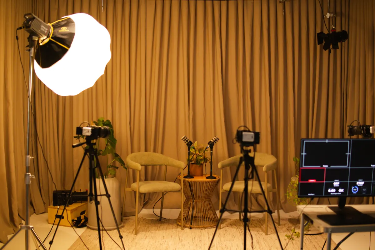 Bastidores: visão do set com refletor, cadeiras, microfones e câmeras em tripés